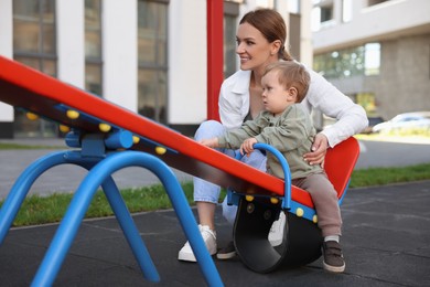 Photo of Happy nanny and cute little boy on seesaw outdoors