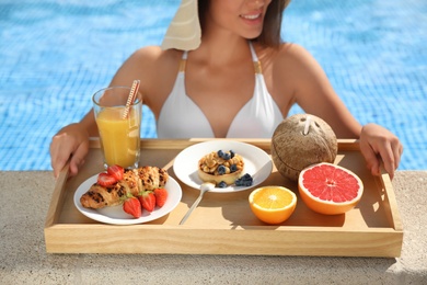 Young woman with delicious breakfast on tray in swimming pool, closeup