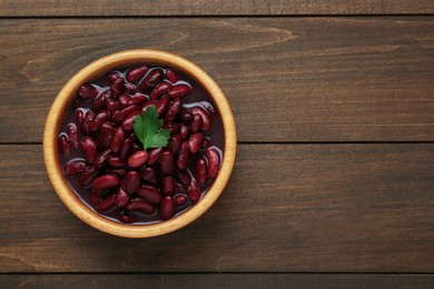 Photo of Bowl of canned red kidney beans with parsley on wooden table, top view. Space for text