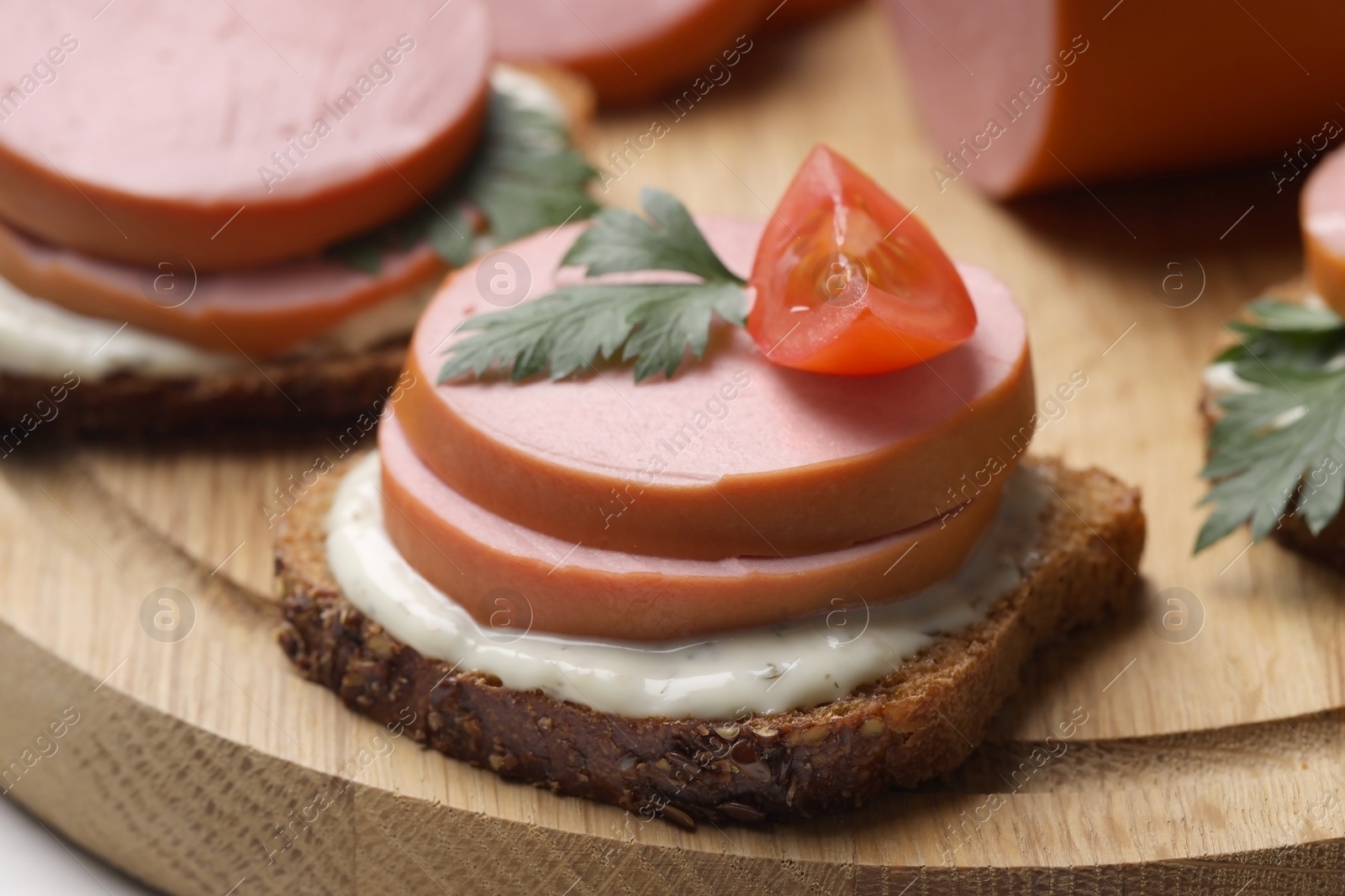 Photo of Delicious sandwich with boiled sausage, tomato and sauce on wooden board, closeup