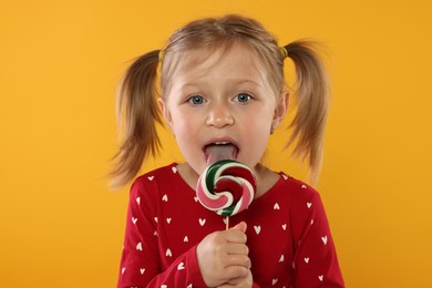Photo of Portrait of cute girl licking lollipop on orange background