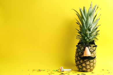 Pineapple with mask, party horn and confetti on yellow background, space for text. Creative concept