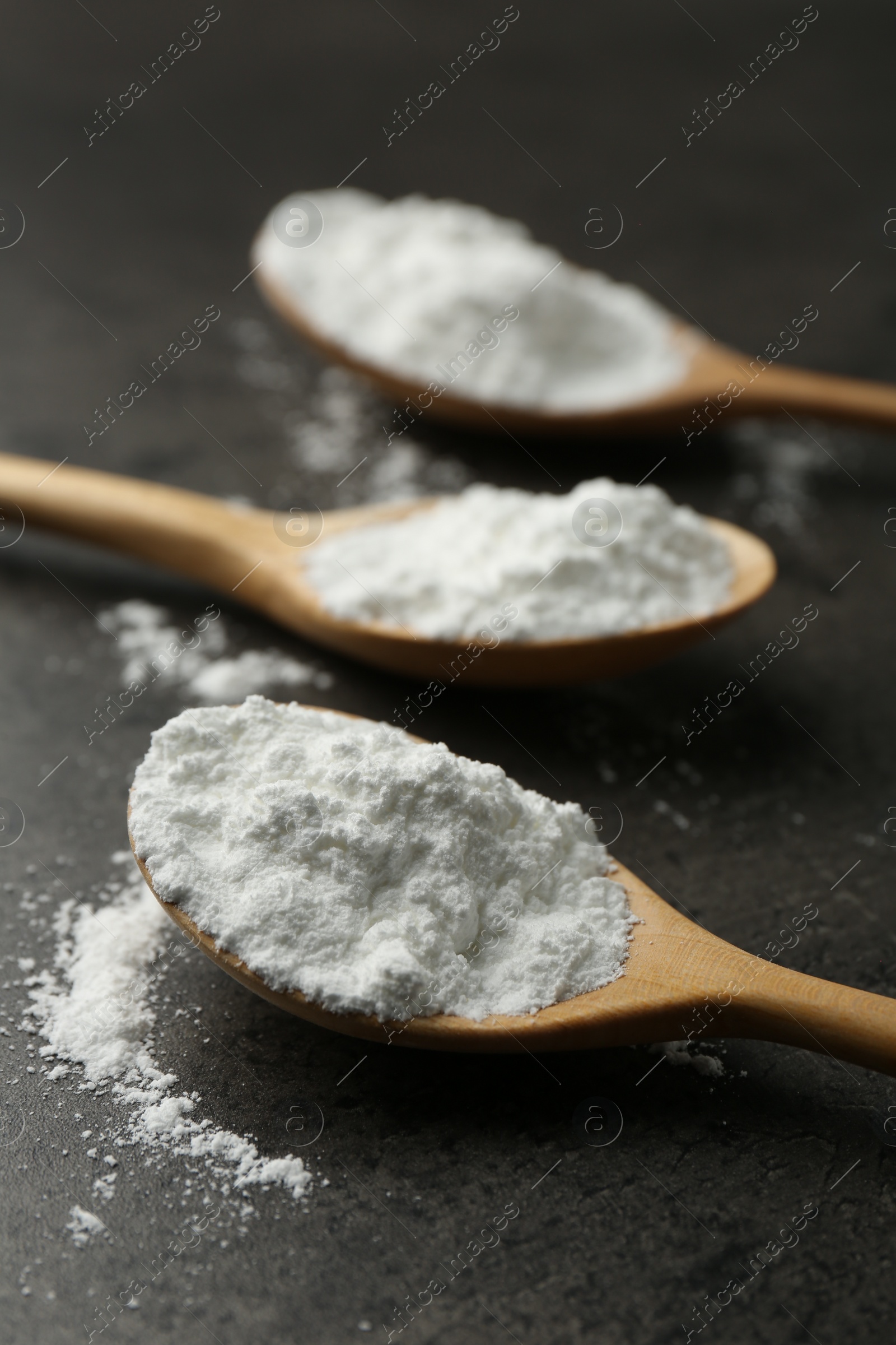 Photo of Baking powder in spoons on grey textured table, closeup