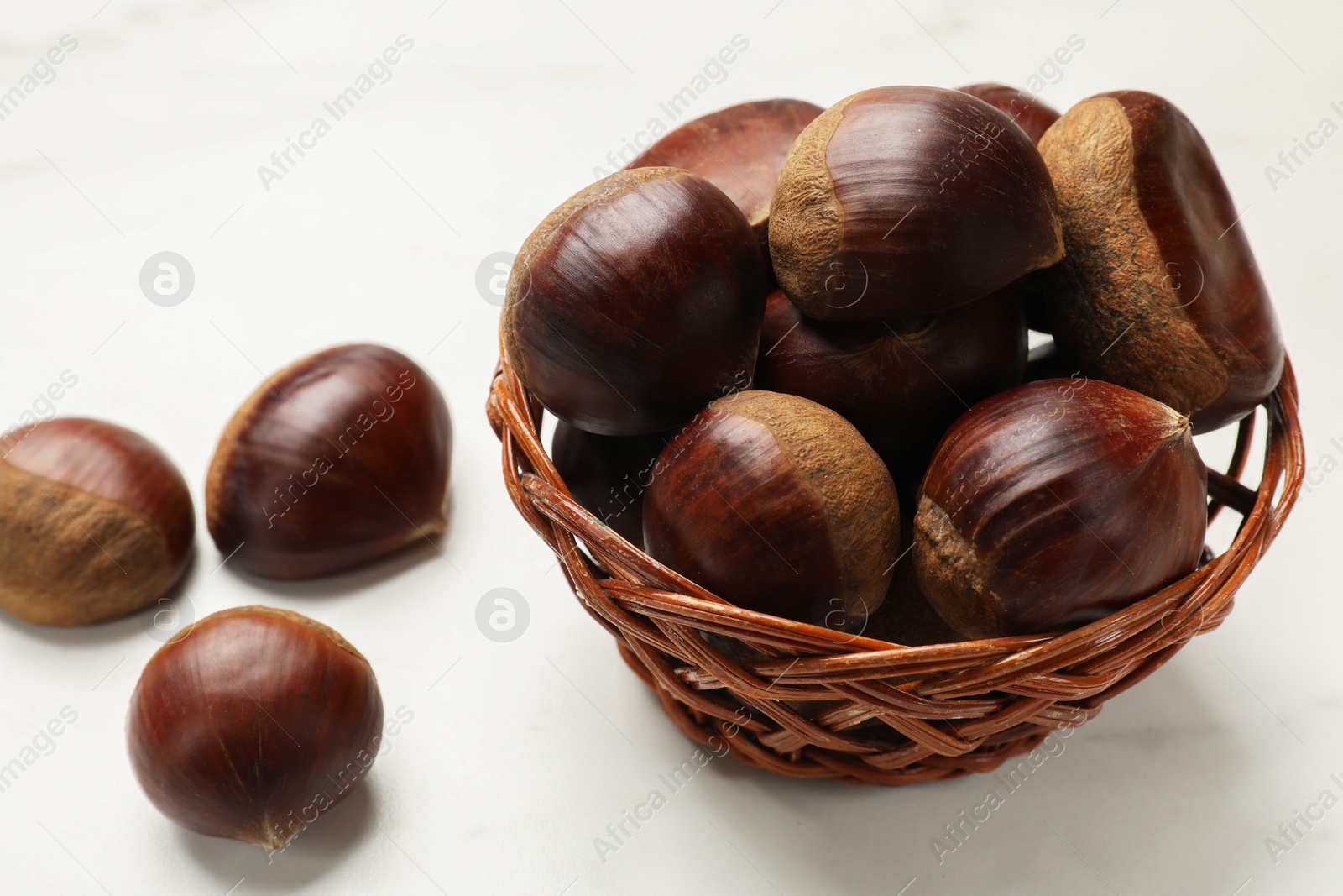 Photo of Sweet fresh edible chestnuts in wicker bowl on white table, closeup