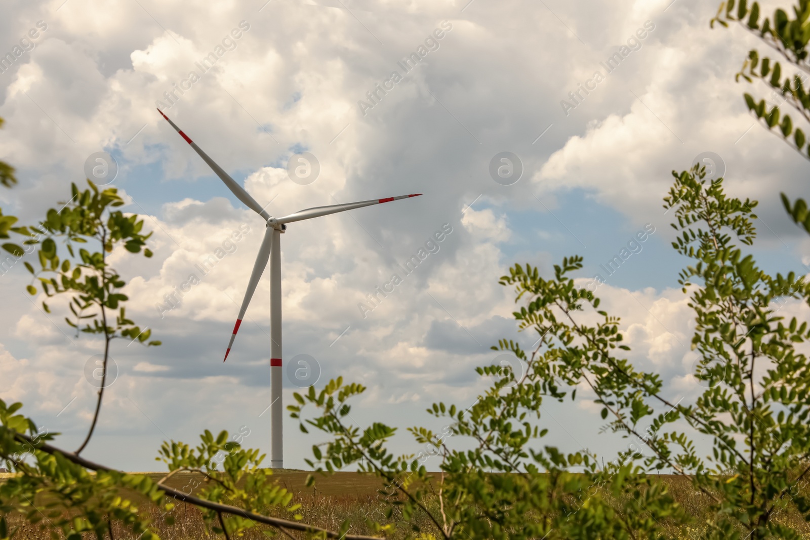 Photo of Modern wind turbine in field on cloudy day. Alternative energy source