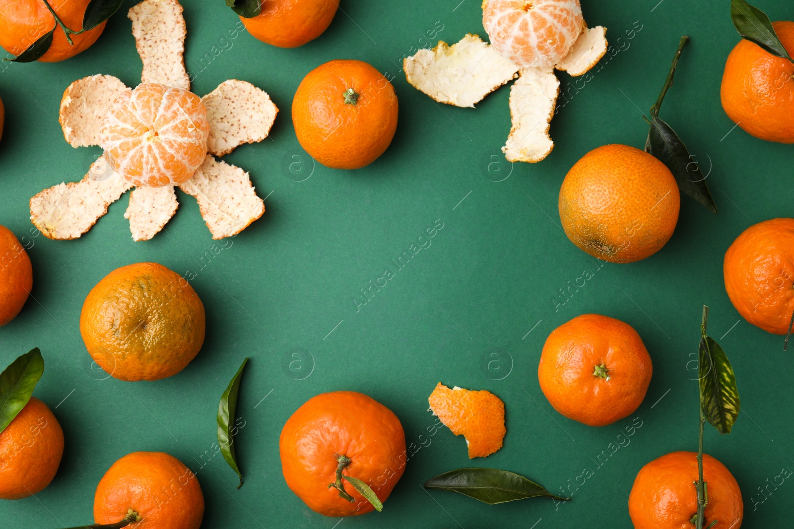 Photo of Frame made of many fresh ripe tangerines and leaves on green table, flat lay. Space for text