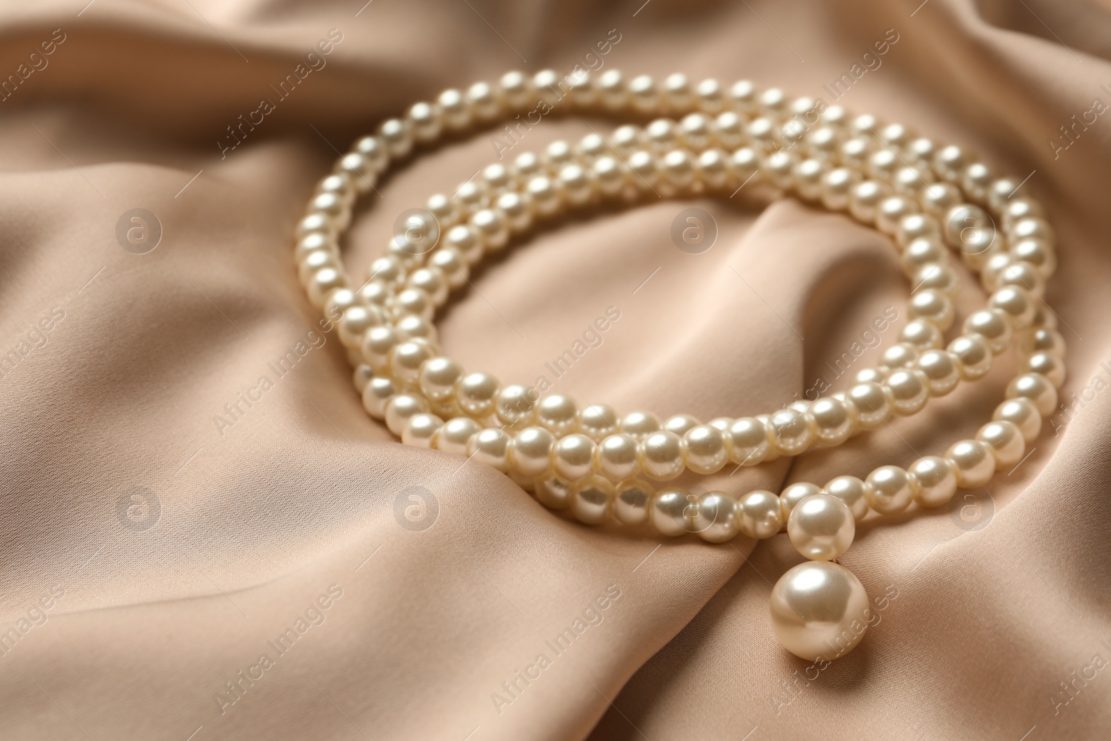 Photo of Elegant necklace with pearls on beige silk, closeup