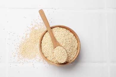 Photo of Dry quinoa seeds and spoon in bowl on white tiled table, top view
