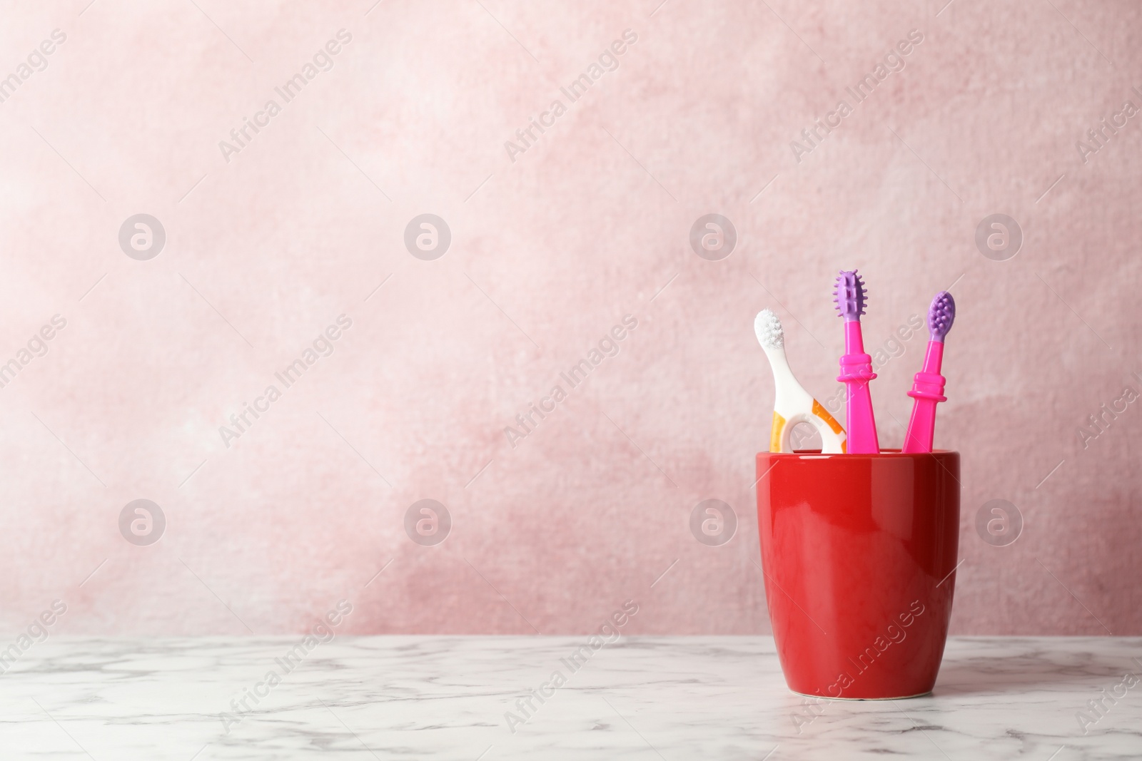 Photo of Baby toothbrushes in holder on table against color background with space for text