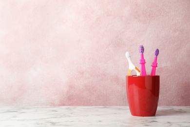 Baby toothbrushes in holder on table against color background with space for text