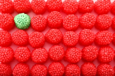 Photo of Delicious green gummy raspberry candy among red ones on pink background, flat lay