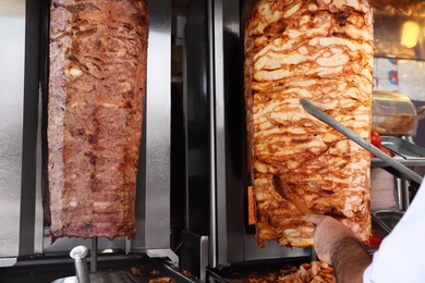 Photo of Man cutting meat from vertical rotisserie, closeup view