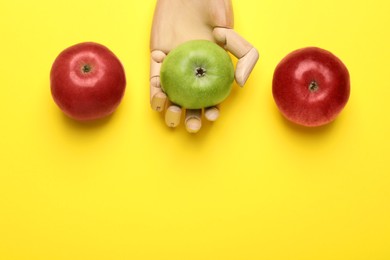 Photo of Mannequin hand with ripe red and green apples on yellow background, flat lay. Space for text