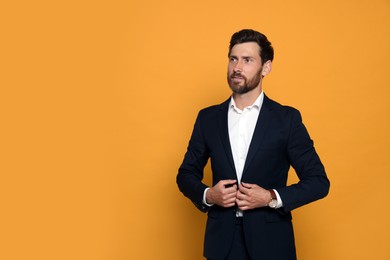 Photo of Elegant bearded man adjusting blazer on orange background. Space for text