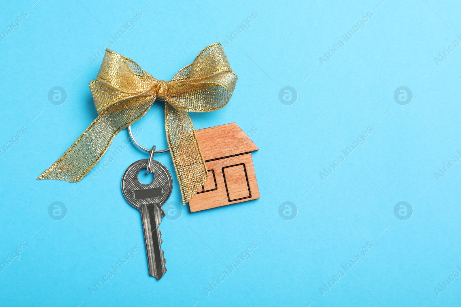 Photo of Key with trinket in shape of house on light blue background, top view and space for text. Housewarming party