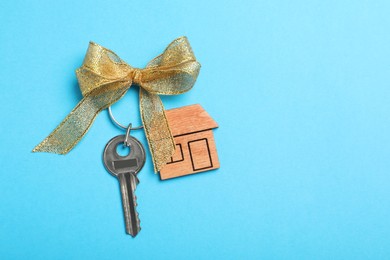 Key with trinket in shape of house on light blue background, top view and space for text. Housewarming party