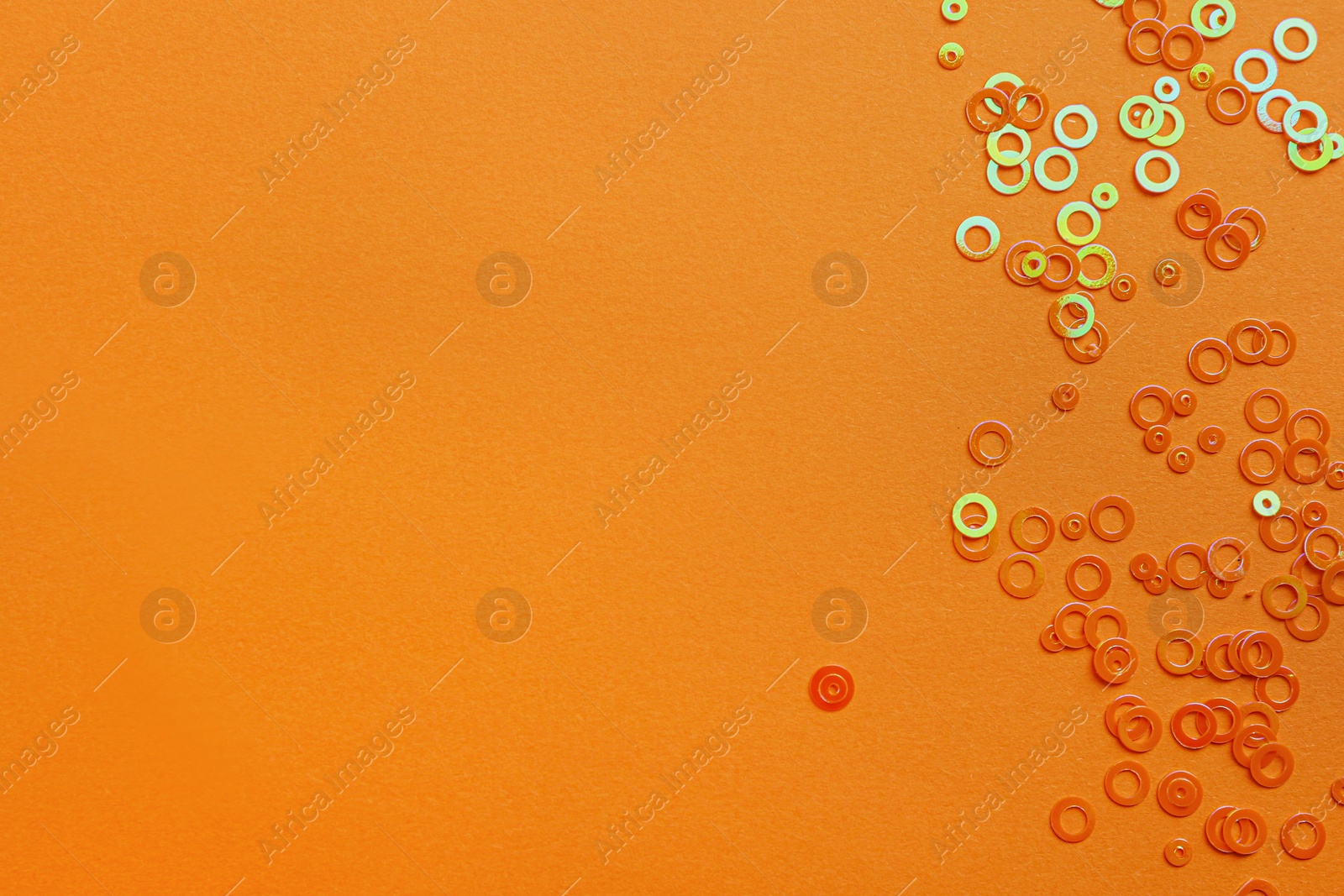 Photo of Shiny bright glitter on orange background, flat lay. Space for text