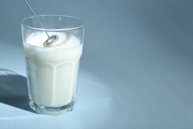 Whisking milk in glass with mini mixer (milk frother) on light blue background, closeup. Space for text