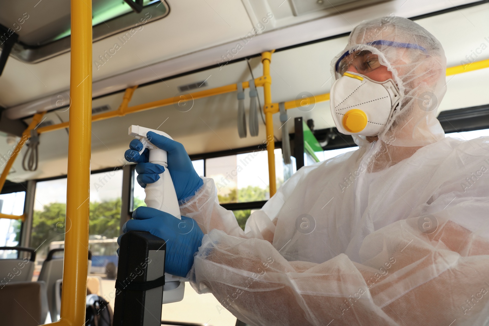 Photo of Public transport sanitation. Worker in protective suit disinfecting bus salon