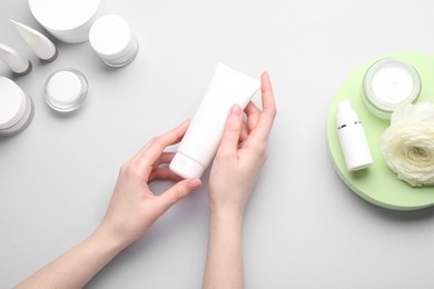 Woman holding tube of cream on light background, top view