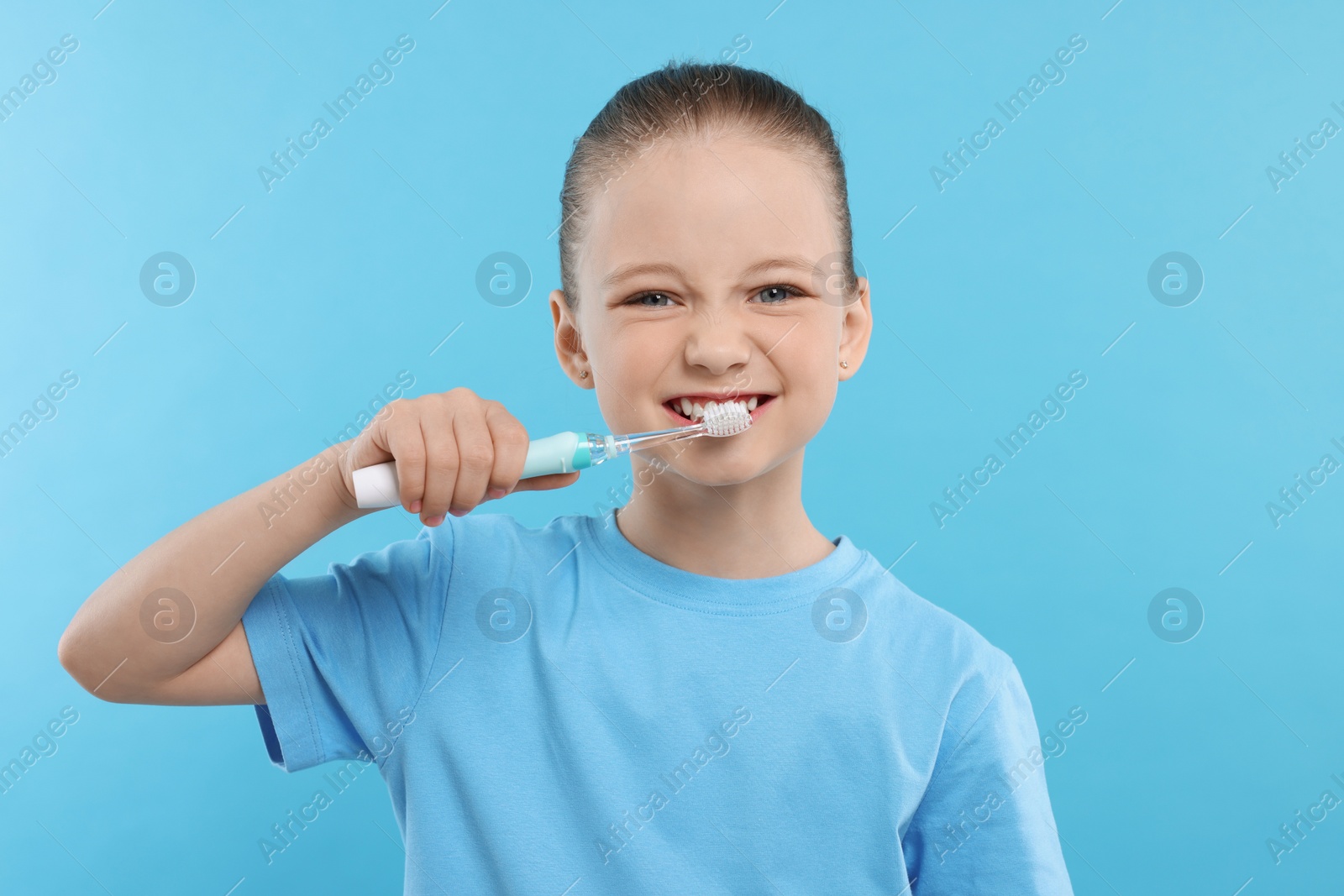 Photo of Happy girl brushing her teeth with electric toothbrush on light blue background