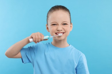 Happy girl brushing her teeth with electric toothbrush on light blue background