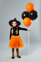 Photo of Cute little girl with balloons wearing Halloween costume on grey background