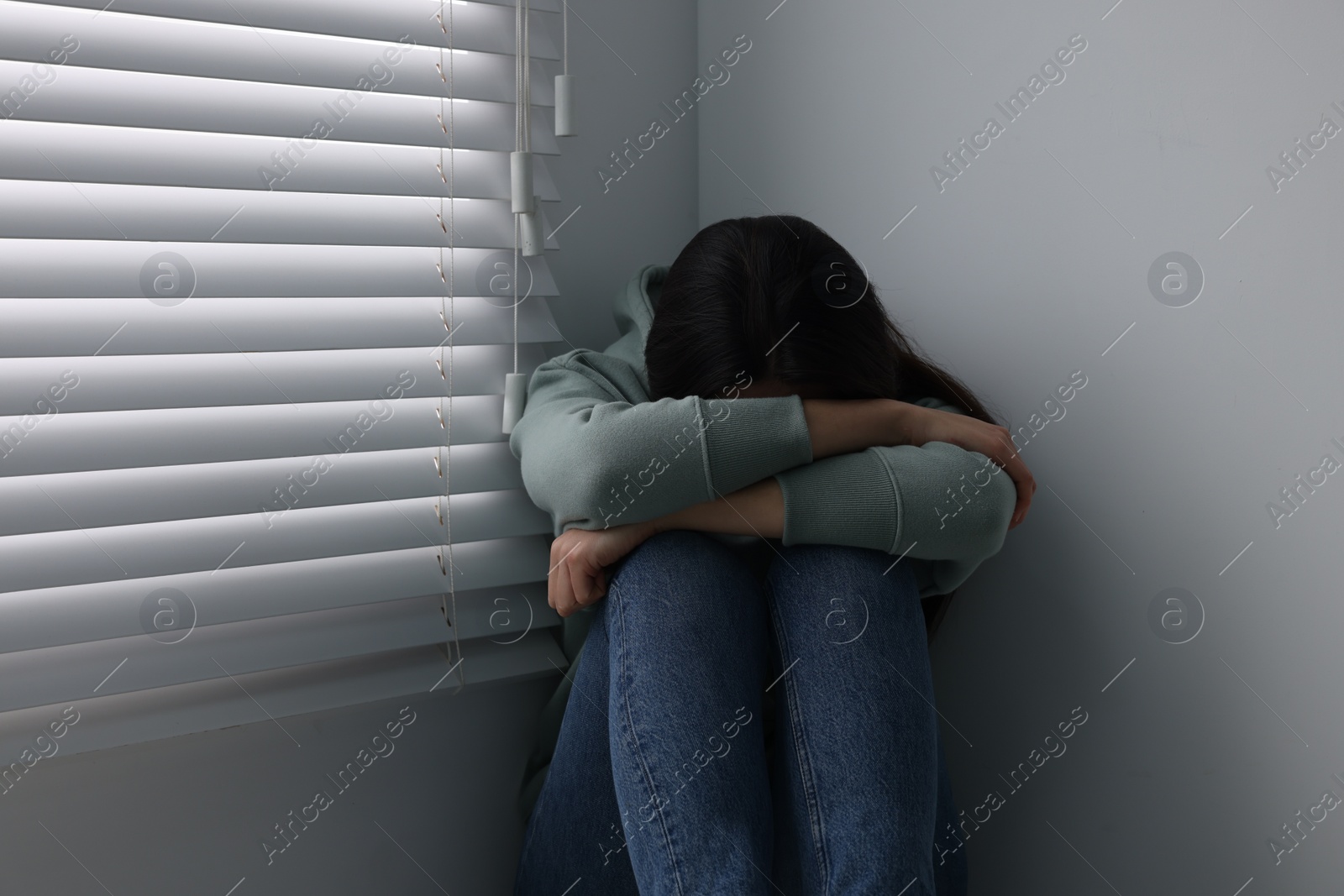 Photo of Sadness. Unhappy woman near window at home