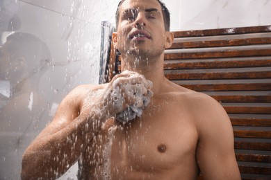 Photo of Man with mesh pouf taking shower at home