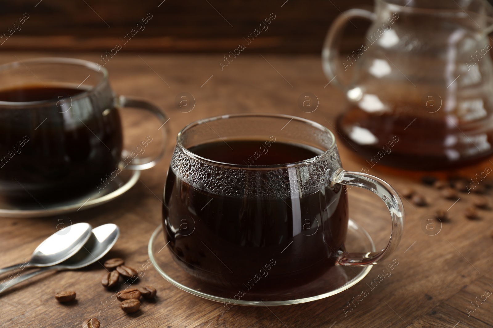 Photo of Hot coffee in glass cups, spoons and beans on wooden table, closeup