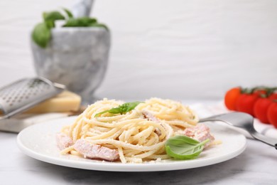 Photo of Plate of tasty pasta Carbonara with basil leaves on white marble table, closeup