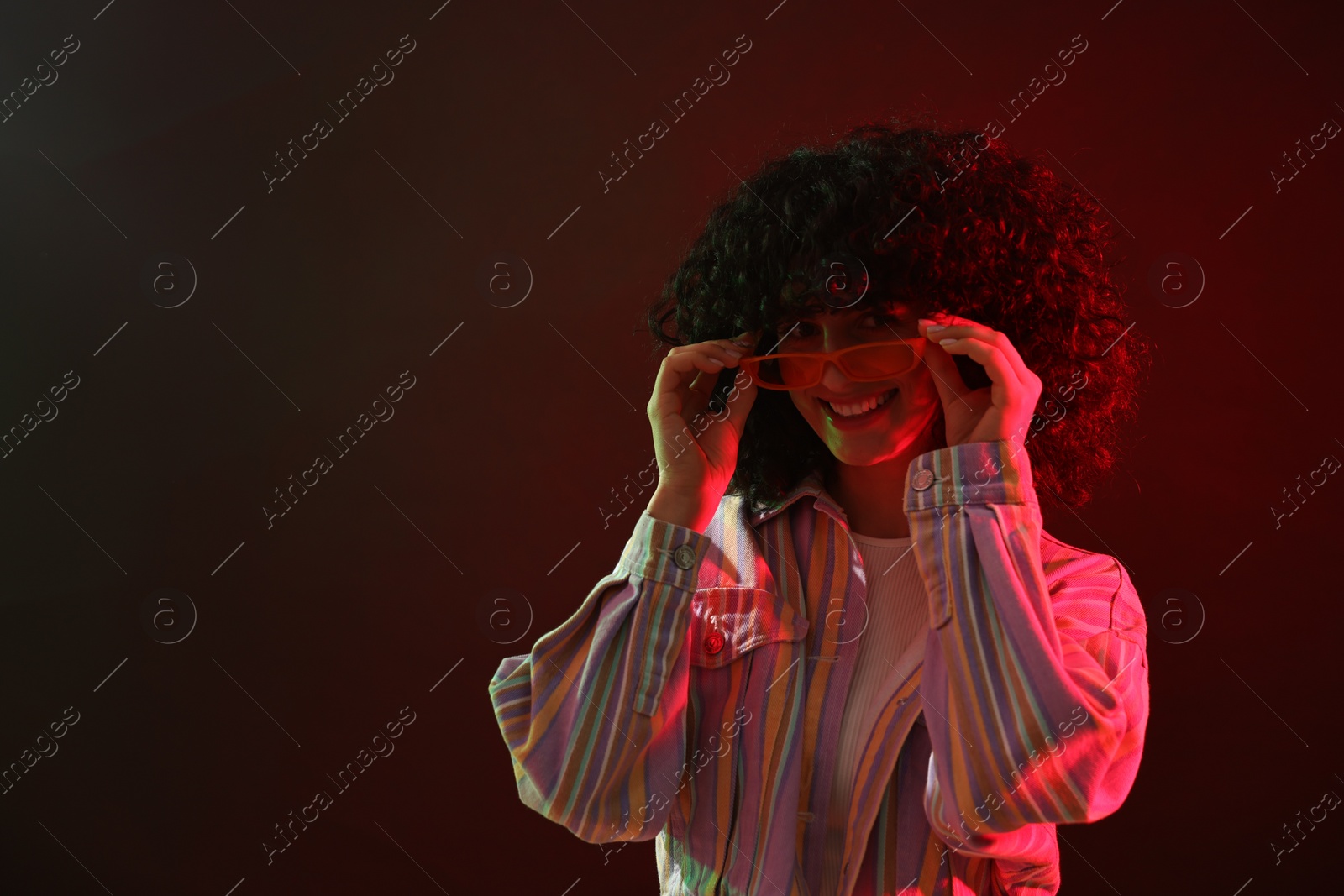 Photo of Beautiful young woman in sunglasses posing on color background in neon lights. Space for text