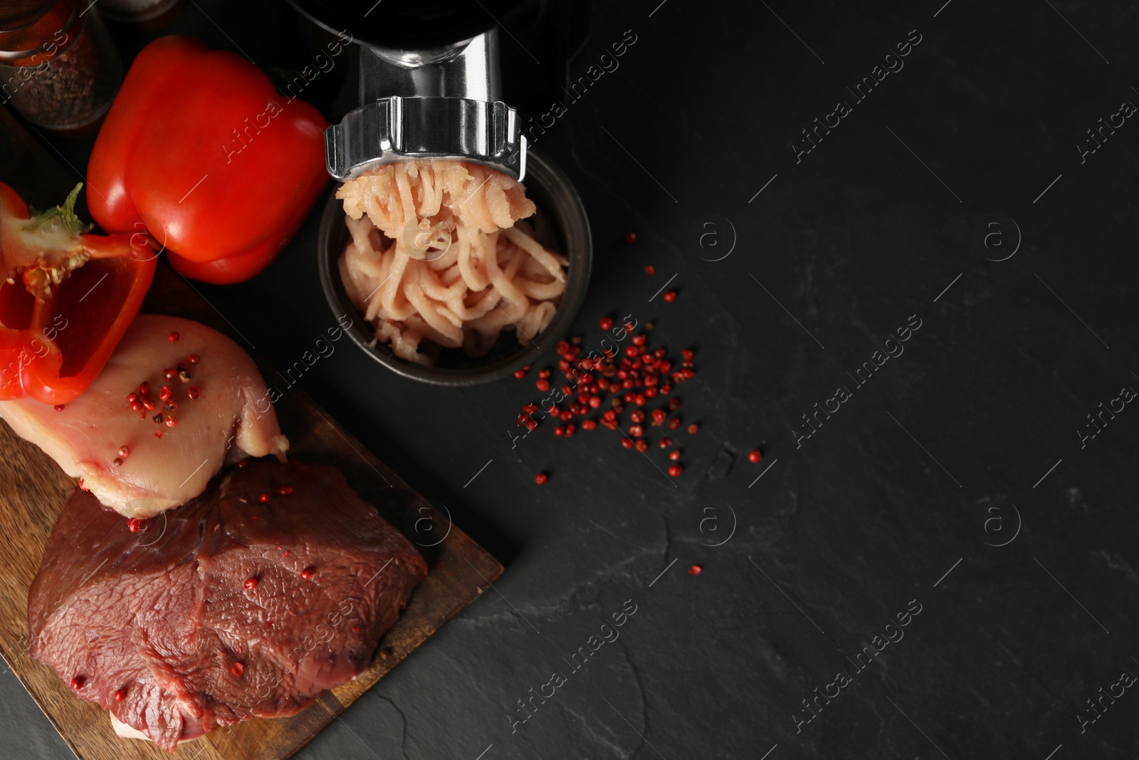 Photo of Electric meat grinder with chicken mince and products on black table, flat lay. Space for text