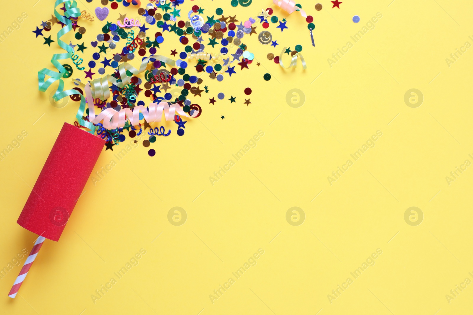 Photo of Colorful confetti and streamers with red party cracker on yellow background, top view. Space for text