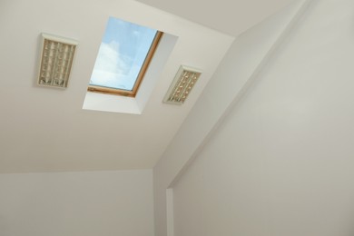 Skylight roof window on slanted ceiling in attic room, low angle view