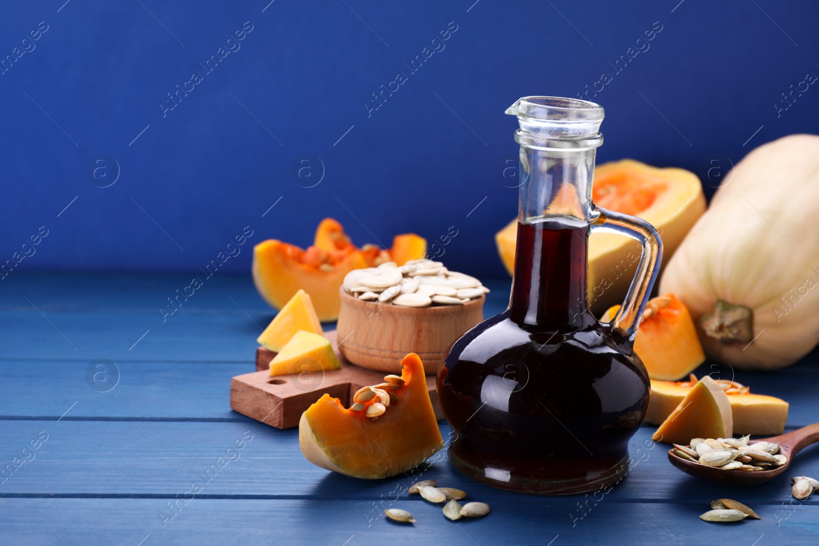 Photo of Fresh pumpkin seed oil in glass jug on blue wooden table. Space for text