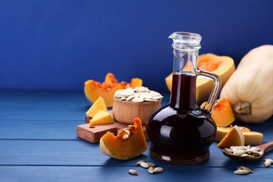 Fresh pumpkin seed oil in glass jug on blue wooden table. Space for text