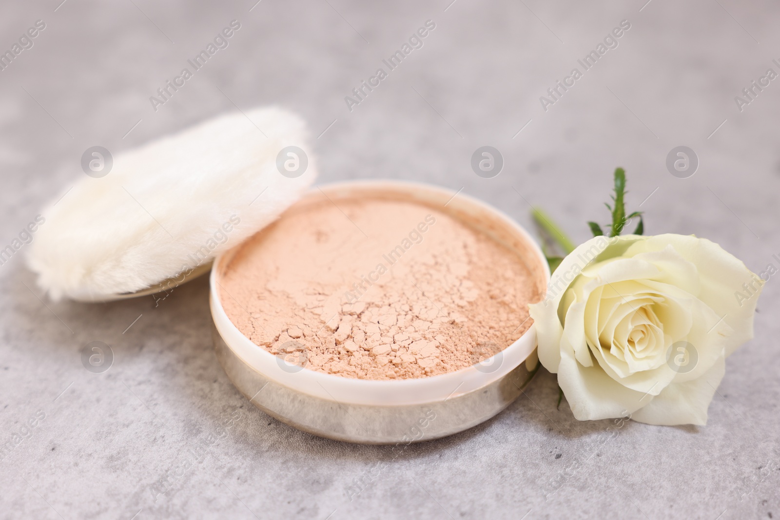 Photo of Face powder, puff applicator and rose flower on grey textured table, closeup