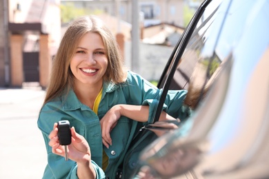 Photo of Young woman with key near new car outdoors