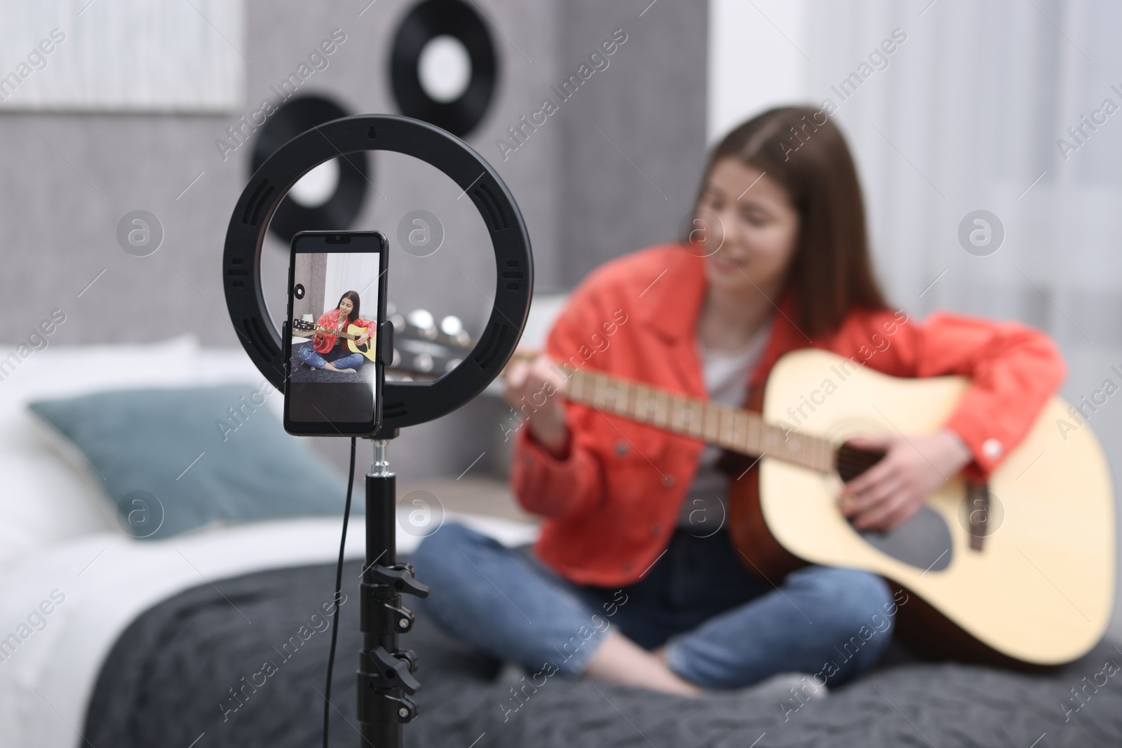 Photo of Teenage blogger playing guitar while streaming at home, focus on smartphone