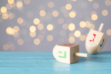 Photo of Hanukkah traditional dreidel with letters Pe and He on wooden table against blurred lights. Space for text