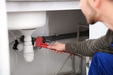 Photo of Male plumber repairing kitchen sink with pipe wrench, closeup