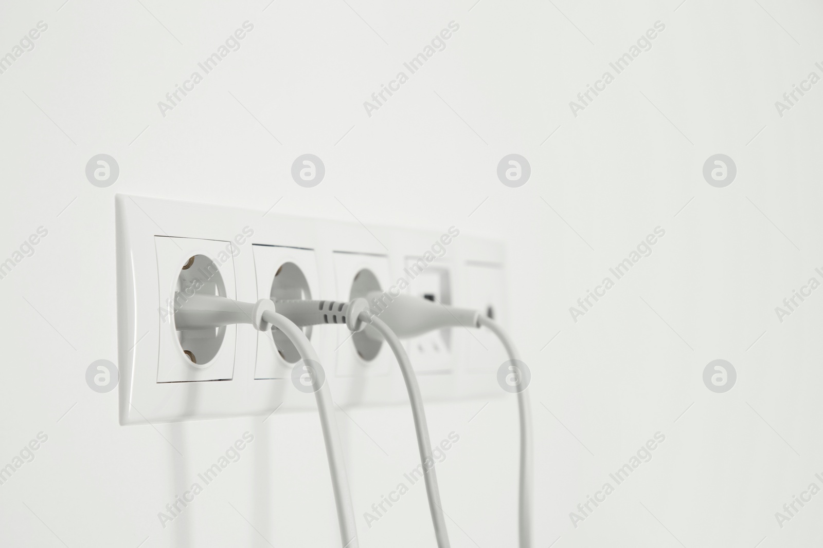 Photo of Many power sockets with plugs on white wall indoors. Space for text
