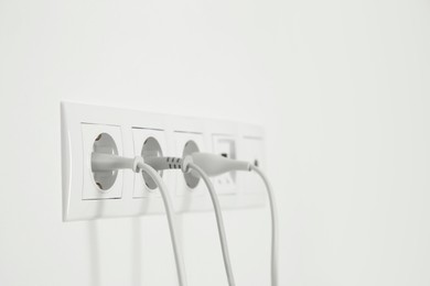 Many power sockets with plugs on white wall indoors. Space for text