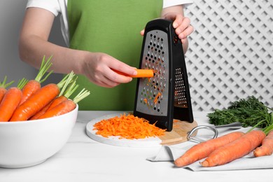 Photo of Woman grating fresh carrot at table indoors, closeup