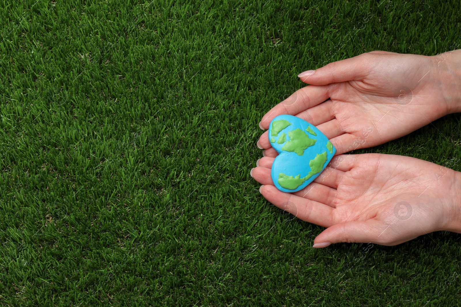 Photo of Happy Earth Day. Woman with heart shaped plasticine planet on green grass, top view and space for text