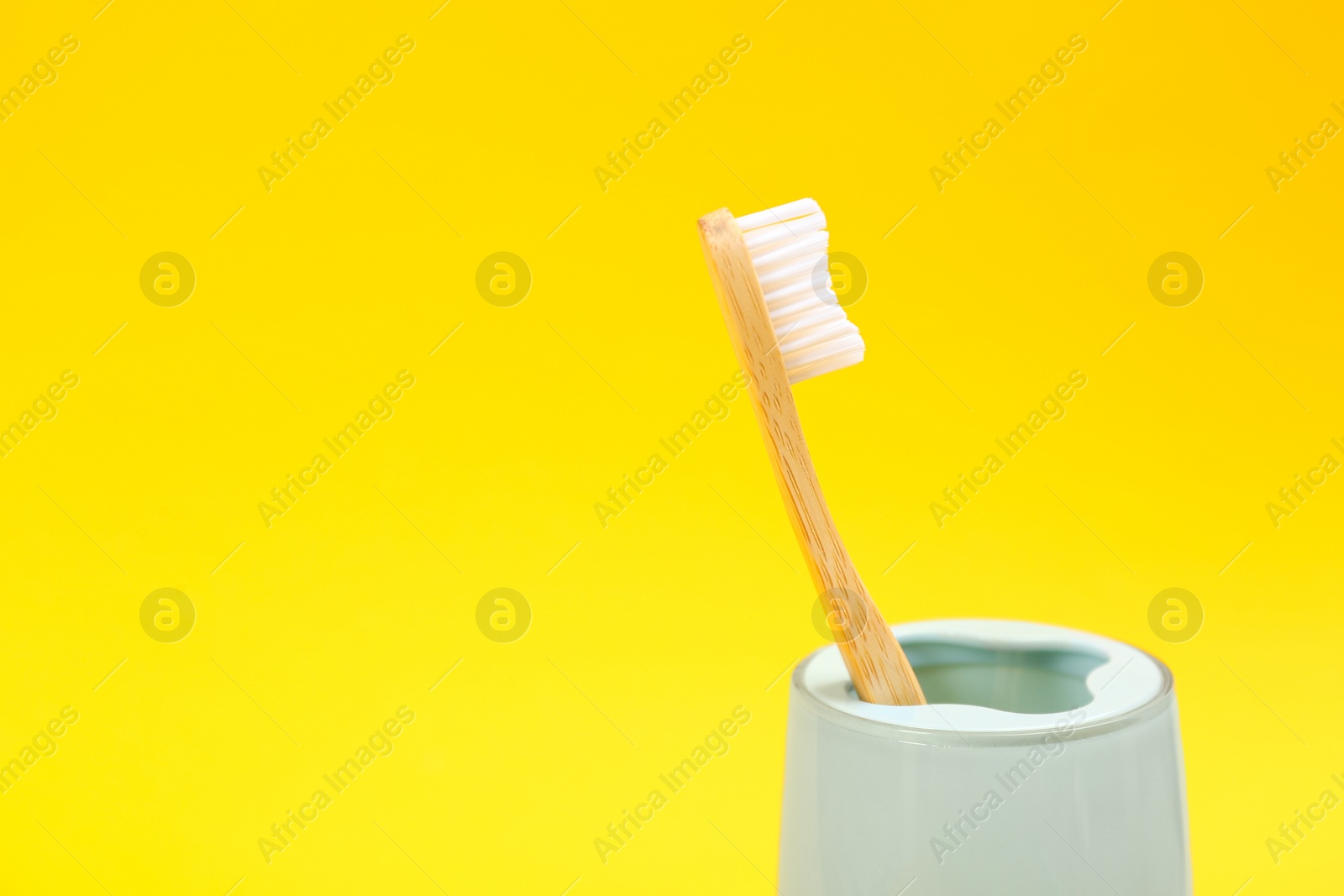 Photo of Toothbrush made of bamboo in holder on yellow background. Space for text