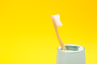Photo of Toothbrush made of bamboo in holder on yellow background. Space for text