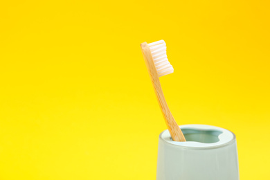 Toothbrush made of bamboo in holder on yellow background. Space for text