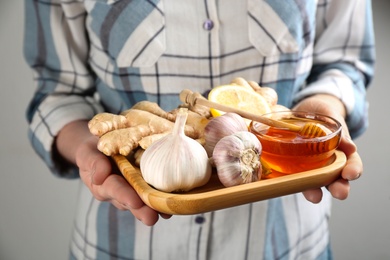 Photo of Woman holding tray with fresh products on grey background, closeup. Natural antibiotics